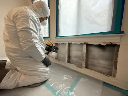 Technician in protective gear working at an opened wall under containment during a sewage cleanup