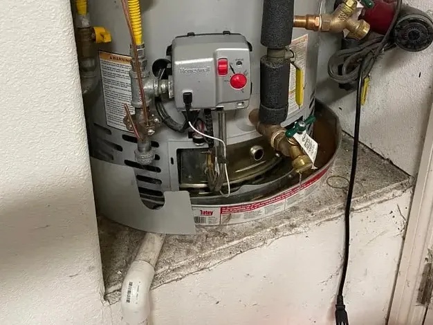 Base of a gas water heater in a closet with its drain pan and supply fittings